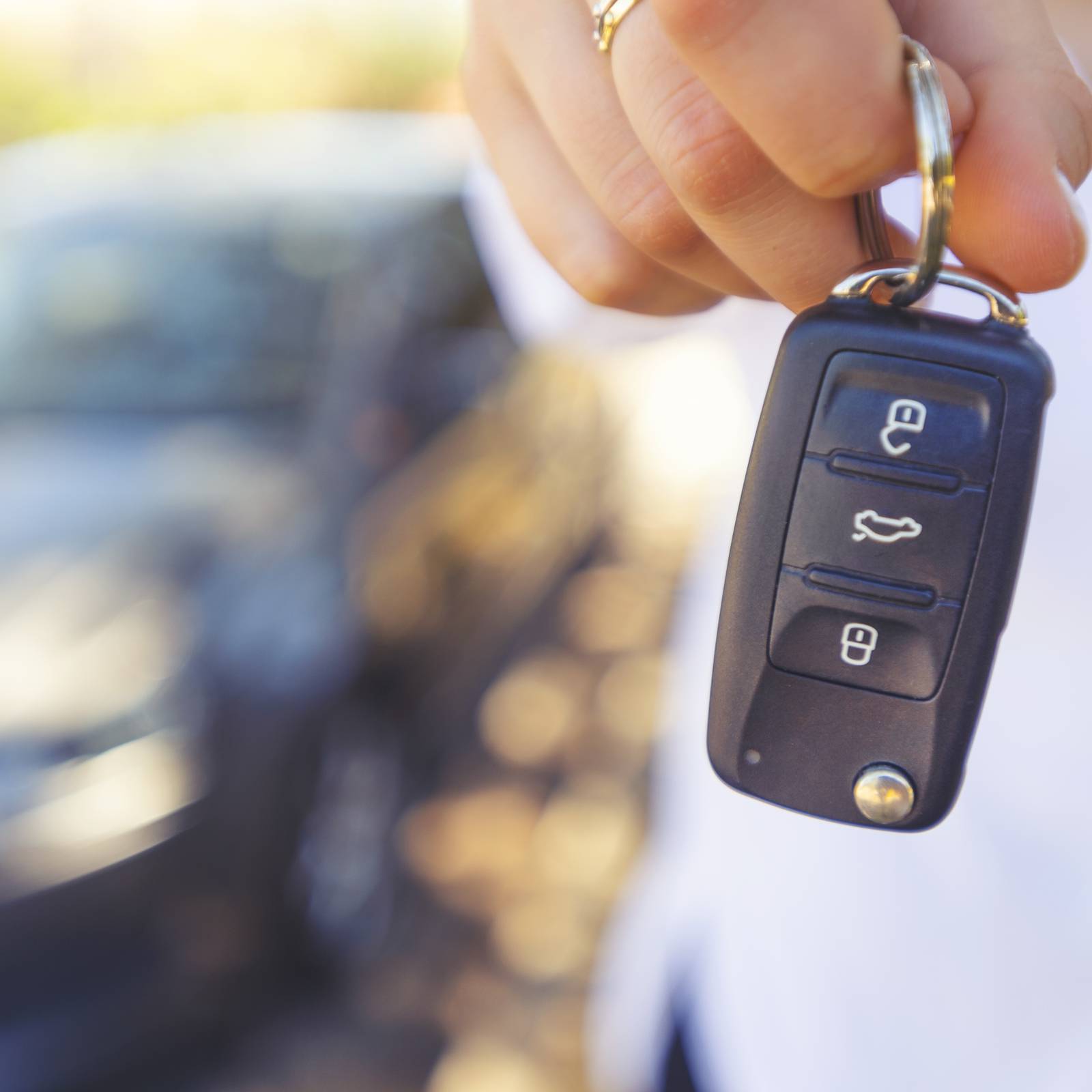 Female car salesperson handing  over the new car keys. There is a new car behind her out of focus. Close up with Copy space